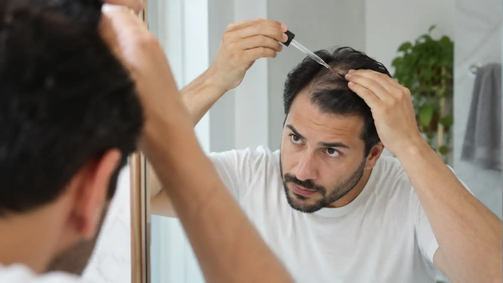 Hombre frente al espejo del baño aplicándose con un gotero un tratamiento con minoxidil en la zona frontal del cuero cabelludo